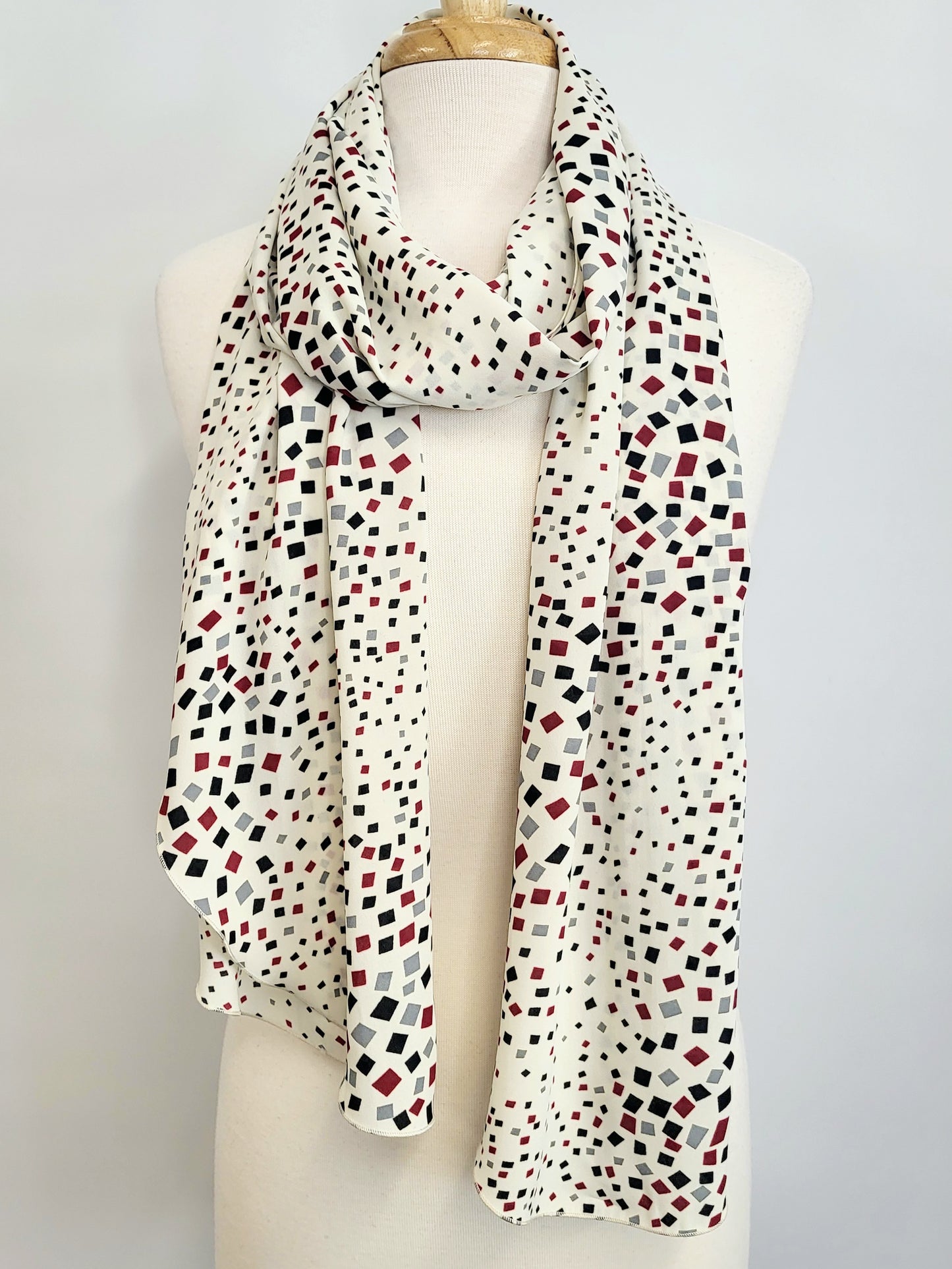 Long scarf printed with small black, gray and burgundy squares on an ecru background.