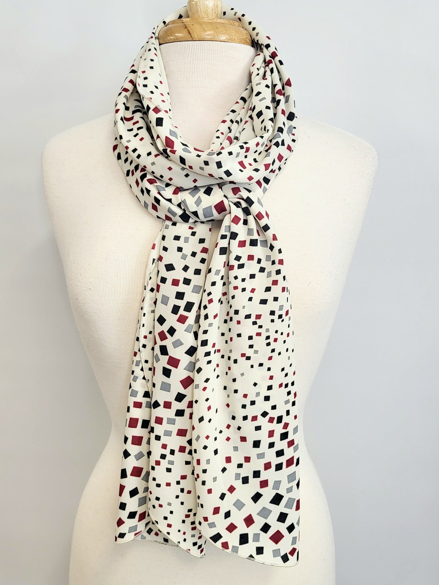 Long scarf printed with small black, gray and burgundy squares on an ecru background.